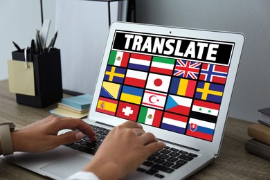 Image of Translator using modern laptop with images of different flags on screen at table in office, closeup