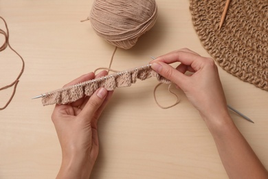 Woman knitting with threads at wooden table, top view. Engaging hobby