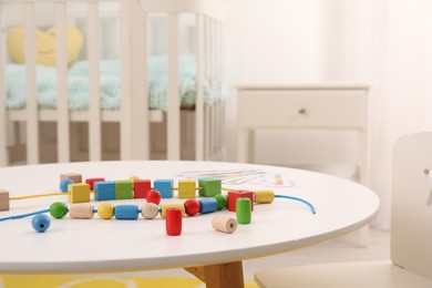 Wooden pieces and string for threading activity on white table indoors. Motor skills development