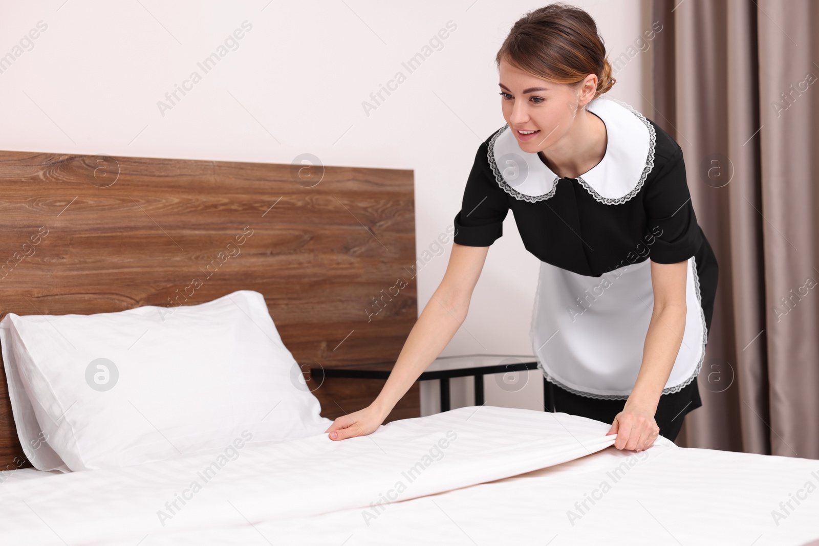 Photo of Beautiful chambermaid making bed in hotel room