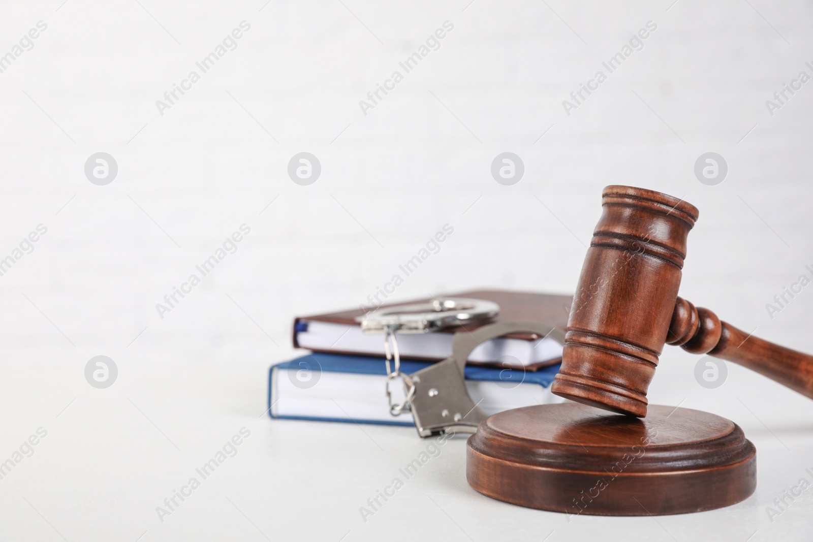 Photo of Gavel, handcuffs and books on white table, space for text. Criminal law