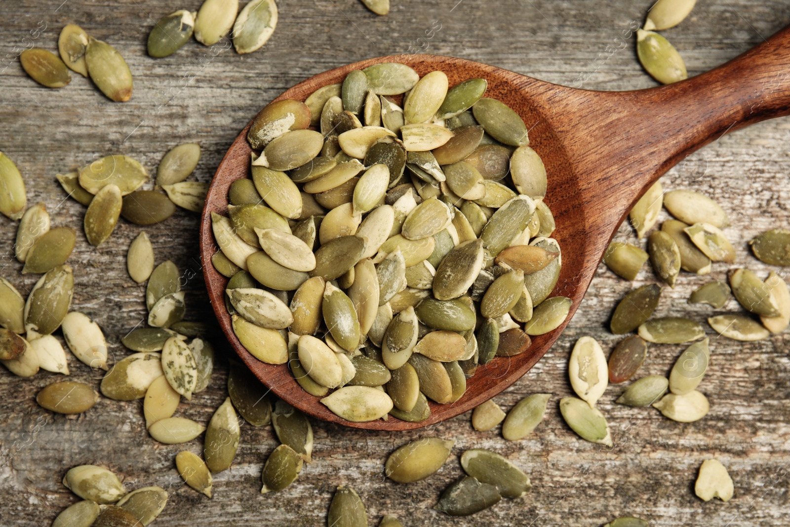 Photo of Spoon with pumpkin seeds on wooden table, flat lay