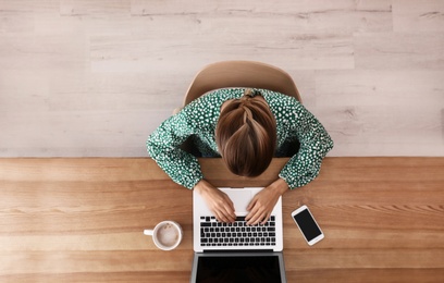 Woman working with laptop at table indoors, top view