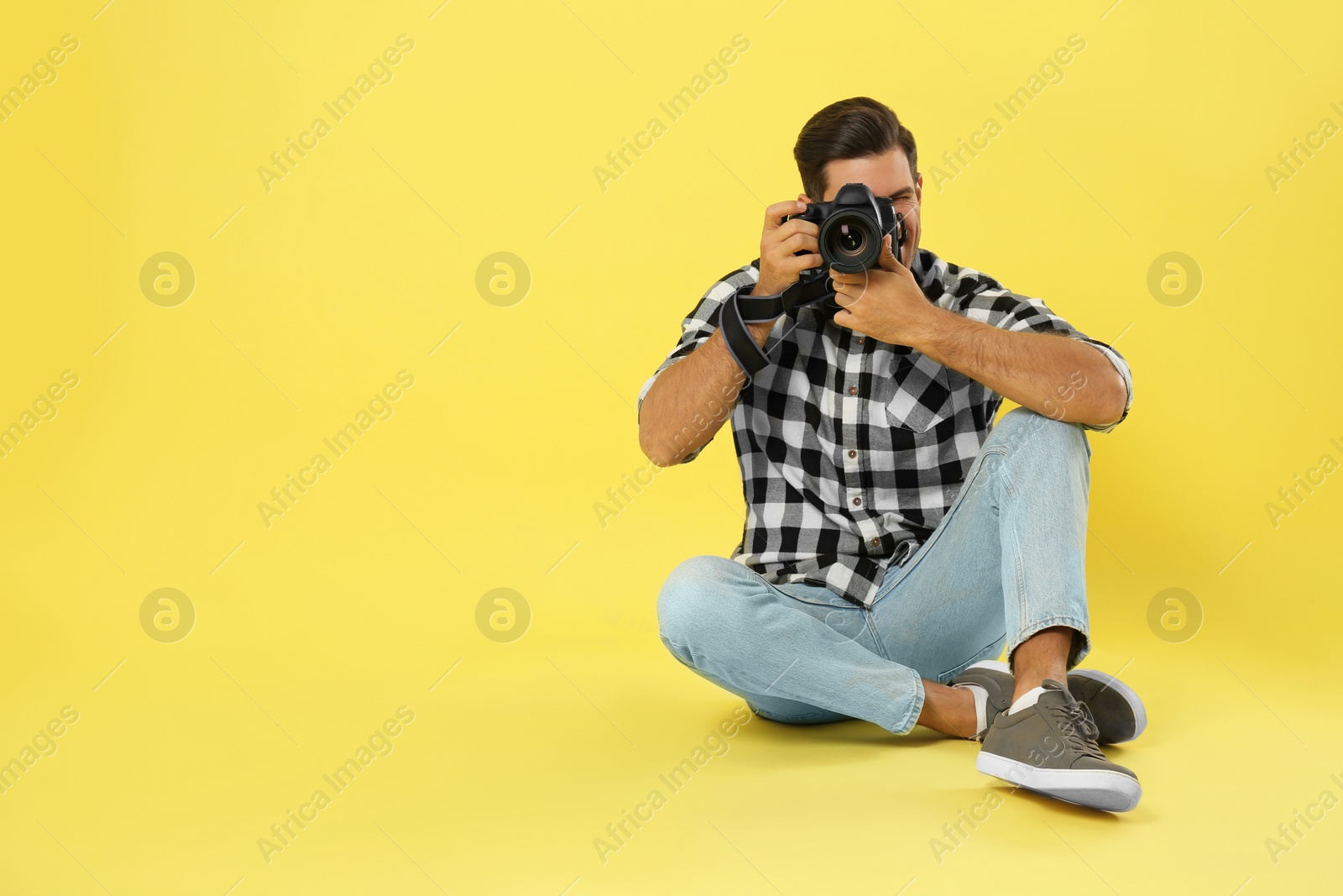 Photo of Professional photographer working on yellow background in studio. Space for text