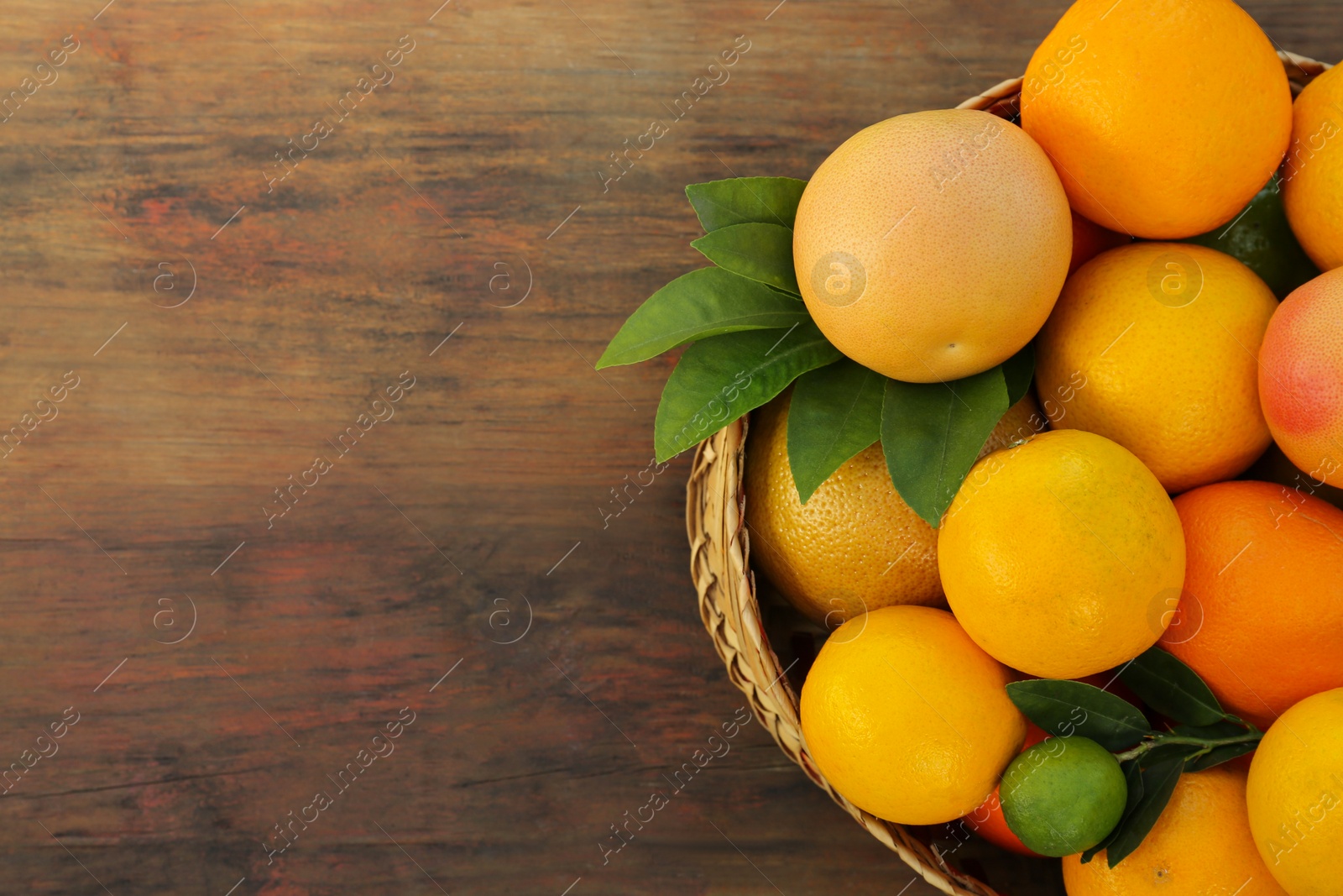 Photo of Wicker basket with different citrus fruits and leaves on wooden table, top view. Space for text