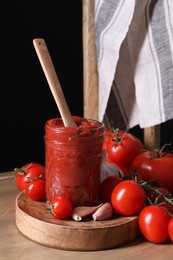 Jar of tasty tomato paste with spoon and ingredients on wooden table