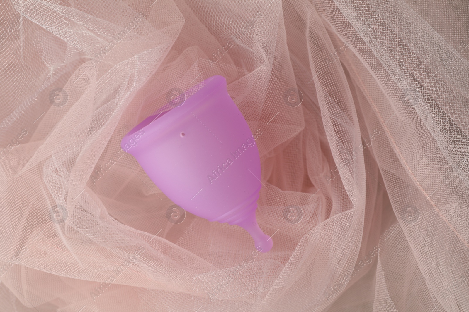 Photo of Menstrual cup on pink fabric, top view
