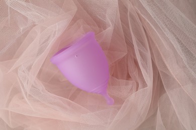 Photo of Menstrual cup on pink fabric, top view