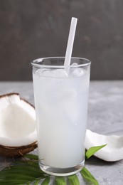 Photo of Glass of coconut water with ice cubes, palm leaf and nut on grey table