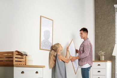 Little girl helping her father to hang painting on wall at home