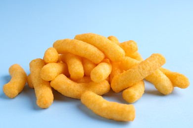 Photo of Heap of tasty cheesy corn puffs on light blue background, closeup view