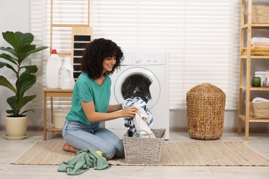 Photo of Happy woman with laundry near washing machine indoors