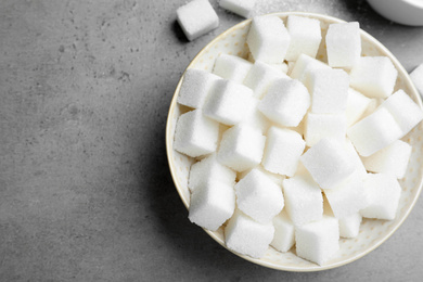 Photo of Refined sugar cubes in bowl on grey table, top view