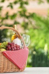 Photo of Picnic basket with products and wine on table against blurred background, space for text