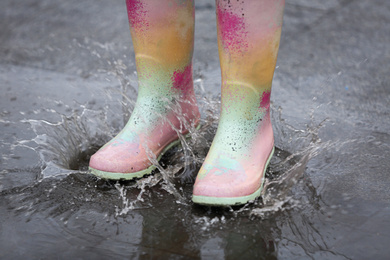 Photo of Woman in rubber boots walking outdoors on rainy day, closeup