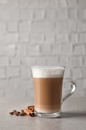 Photo of Glass cup of delicious layered coffee, beans and cinnamon on light grey table near white wall, space for text