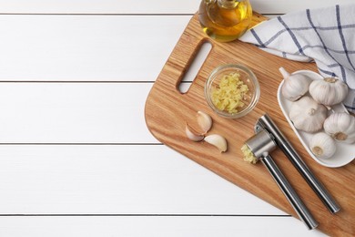 Photo of Board with metal press and garlic on white wooden table, top view. Space for text