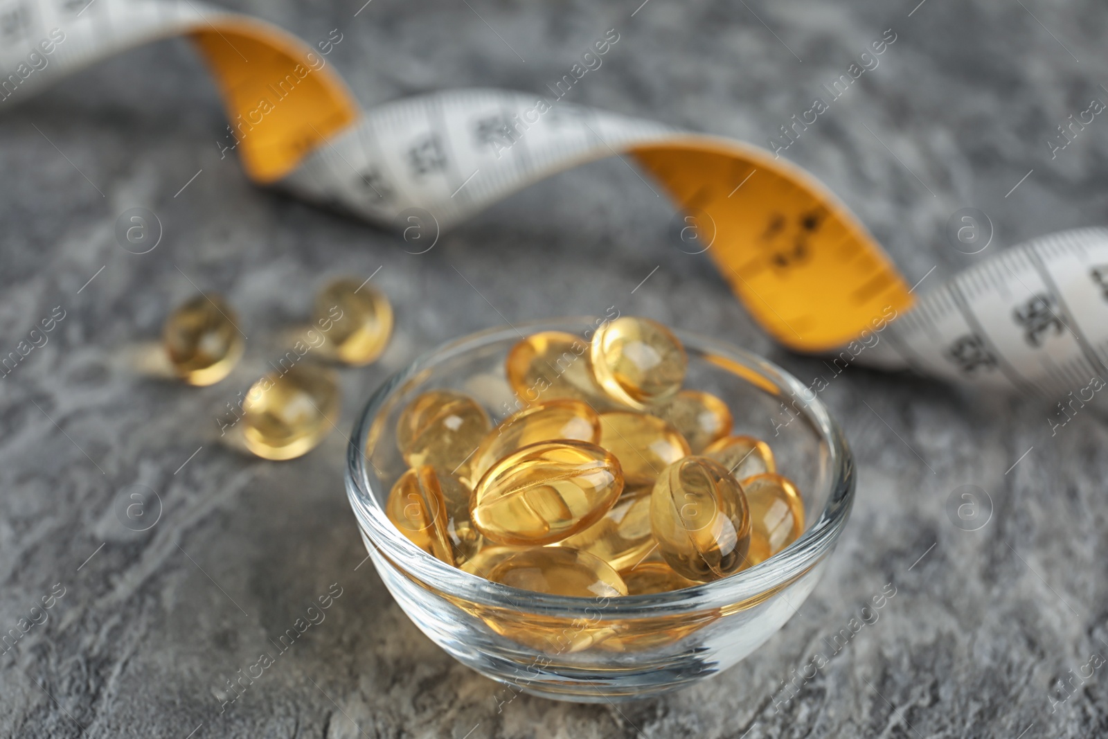 Photo of Cod liver oil pills and measuring tape on gray background, closeup