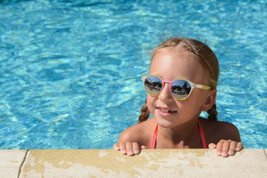 Photo of Happy cute little girl with sunglasses at edge of swimming pool on sunny day. Space for text