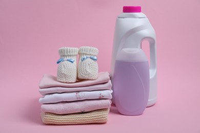 Photo of Laundry detergents, stack of baby clothes and small booties on pink background