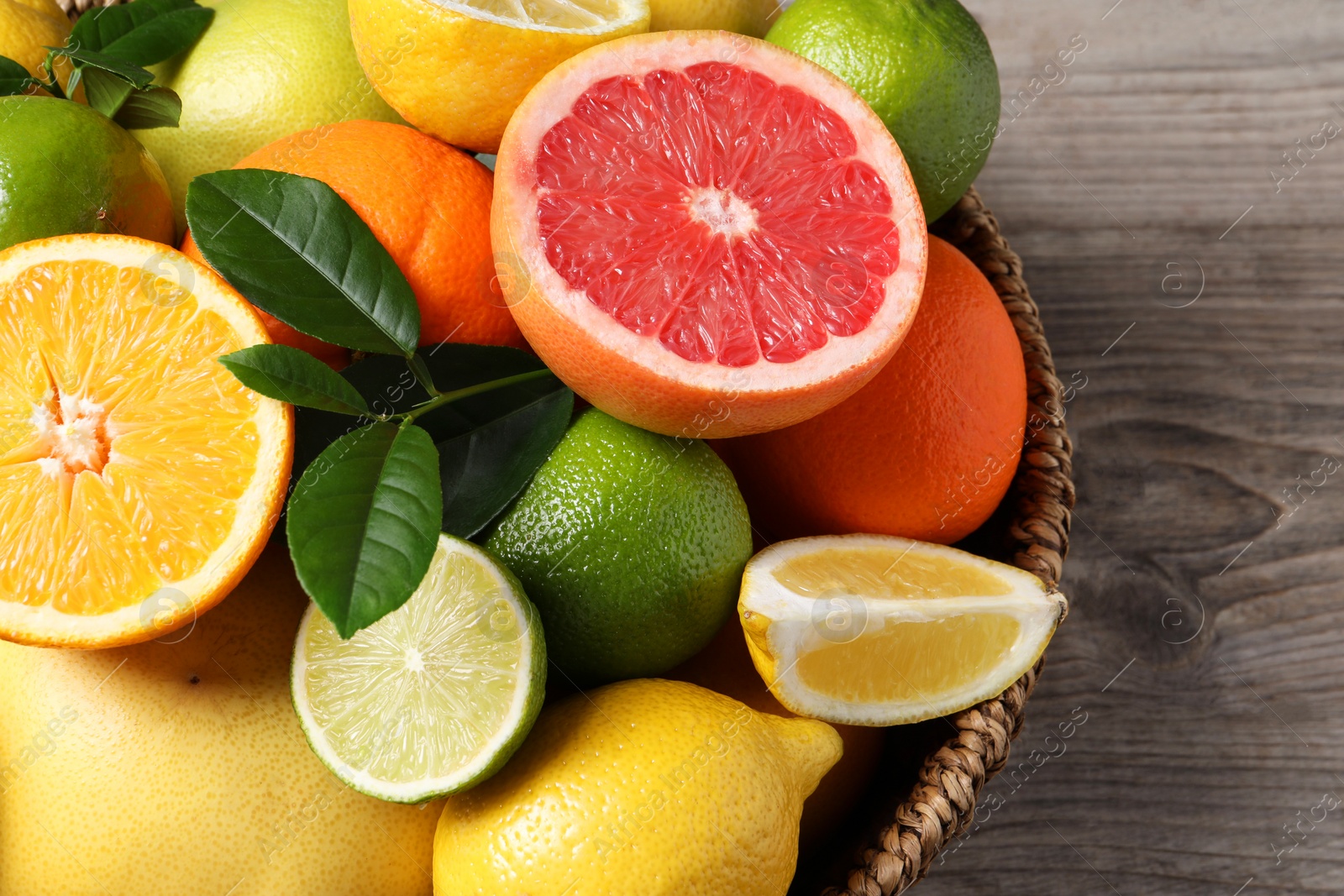 Different fresh citrus fruits and leaves in wicker basket on wooden table, above view Photo of Different fresh citrus fruits and leaves in wicker basket on wooden table, above view