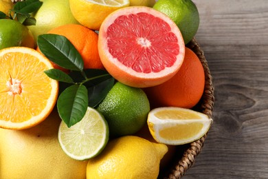 Photo of Different fresh citrus fruits and leaves in wicker basket on wooden table, above view