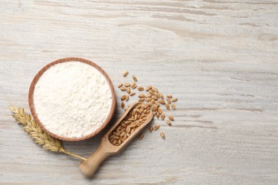 Photo of Organic flour in bowl, scoop with grains of wheat and spikelet on wooden table, flat lay. Space for text