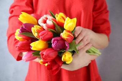 Photo of Woman holding beautiful spring tulips on light blue background, closeup