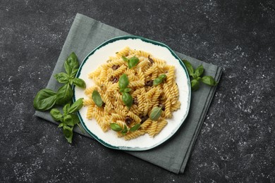 Photo of Plate of delicious pasta with anchovies and basil on black textured table, flat lay