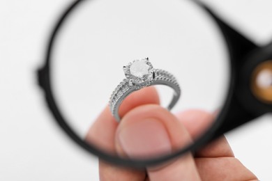 Photo of Jeweler examining diamond ring with magnifying glass on white background, closeup
