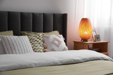 Photo of Comfortable bed with cushions, lamp and different decor on wooden bedside table in room. Stylish interior