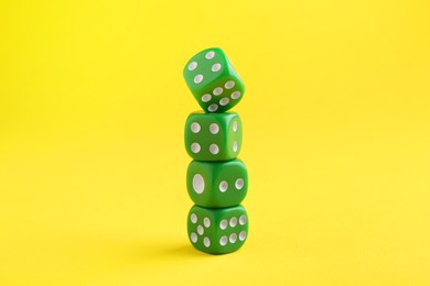 Photo of Many stacked green game dices on yellow background, closeup
