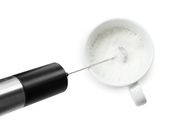 Photo of Whisking milk in cup with mini mixer (frother wand) isolated on white, top view