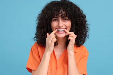 Photo of Young woman applying whitening strip on her teeth against light blue background