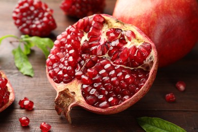 Photo of Cut fresh pomegranate and green leaves on wooden table, closeup