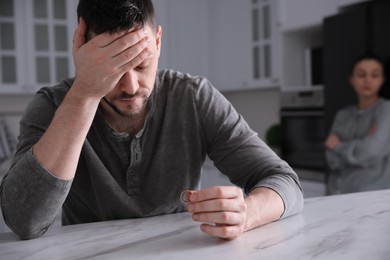 Photo of Sad man with wedding ring in kitchen. Couple on verge of divorce