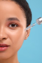 Photo of Woman applying serum onto her face on light blue background, closeup