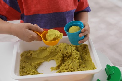 Photo of Little boy playing with bright kinetic sand at table indoors, closeup