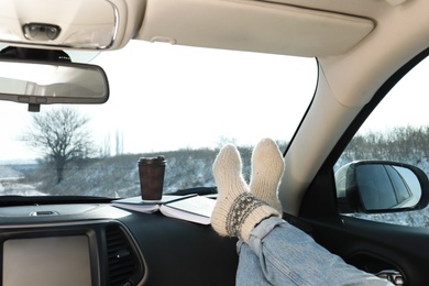 Photo of Young woman in warm socks holding her legs on car dashboard. Cozy atmosphere