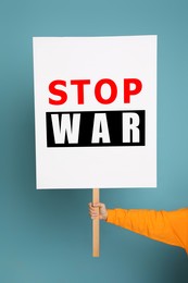 Image of Woman holding poster with words Stop War on light blue background, closeup