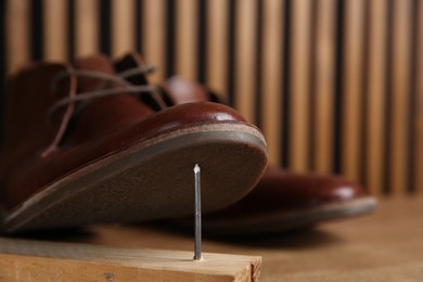 Photo of Metal nail in wooden plank and shoes on table, closeup