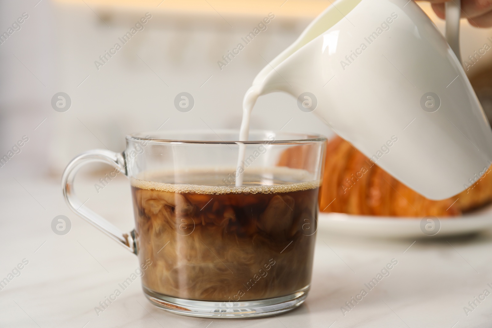 Photo of Pouring milk in coffee at white table, closeup