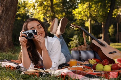 Photo of Happy young woman with camera on plaid in park. Summer picnic