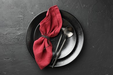 Photo of Stylish setting with cutlery, napkin and plates on dark textured table, top view