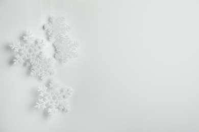Photo of Beautiful decorative snowflakes hanging on light grey background, space for text