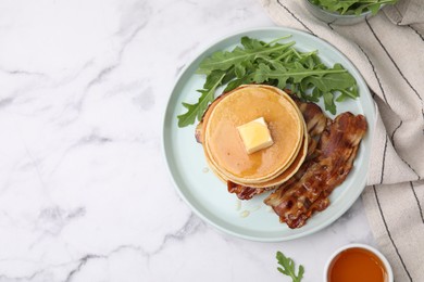 Photo of Tasty pancakes with butter, fried bacon and fresh arugula on white marble table, flat lay. Space for text