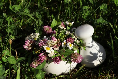 Photo of Ceramic mortar with pestle, different wildflowers and herbs on green grass outdoors