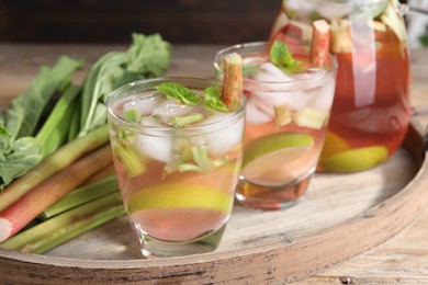 Photo of Tasty rhubarb cocktail with citrus fruits and stems on wooden table