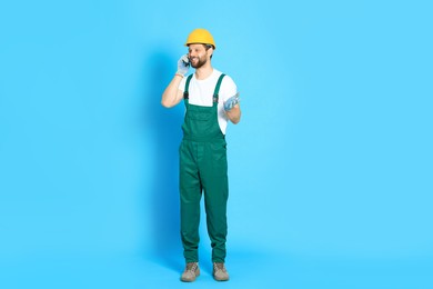 Photo of Professional repairman in uniform talking on smartphone against light blue background