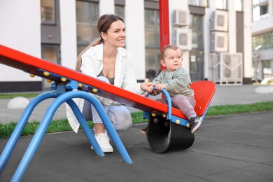 Photo of Happy nanny and cute little boy on seesaw outdoors